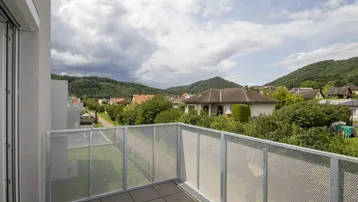Geräumiger Balkon mit Fliesenboden und weitem Blick auf die grüne Umgebung und Berge.