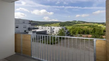 Geräumiger Balkon mit Metallgeländer und weitem Blick über die grüne Hügellandschaft.
