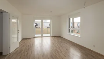 Helles, leeres Wohnzimmer mit Laminatboden und Zugang zu einem Balkon.