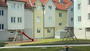 Grüner Innenhof mit Kinderspielplatz, Rutsche und Schaukeln, umgeben von Wohngebäuden.