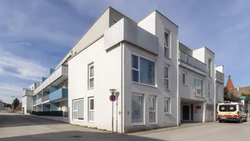 Modernes Mehrfamilienhaus mit weißer Fassade, großen Fenstern und Balkonen an einer Straße.