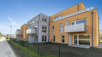 Moderne Wohnanlage mit orangefarbenen und grauen Fassaden sowie Balkonen und Grünflächen.