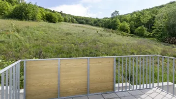 Balkon mit Fliesenboden und Blick auf die grüne Hügellandschaft unter blauem Himmel.