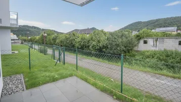 Geflieste Terrasse im Erdgeschoss mit Blick ins Grüne und umzäuntem Gartenbereich.