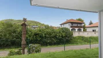 Blick von einer Terrasse auf grüne Hügel und ein traditionelles Haus in der Ferne.