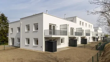 Moderne Wohngebäude mit weißer Fassade und Balkonen in einer ländlichen Umgebung.