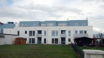 Rückansicht eines modernen Wohngebäudes mit weißer und blauer Fassade sowie einem Gartenbereich.
