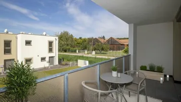 Gemütlicher Balkon mit Sitzgelegenheiten und Blick auf die ländliche Umgebung und andere Gebäude.