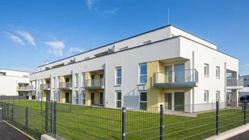 Modernes Mehrfamilienhaus mit weißer Fassade, Balkonen und gepflegter Rasenfläche.