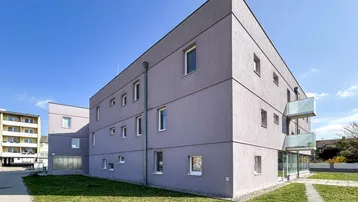 Modernes Mehrfamilienhaus mit schlichter Fassade und kleinen Balkonen unter blauem Himmel.