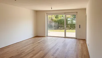 Helles, leeres Zimmer mit Holzboden und Zugang zu einer Terrasse oder Garten.