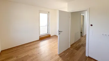 Helles Zimmer mit Holzboden und Zugang zu einem Balkon oder einer Terrasse, bereit zum Einzug.