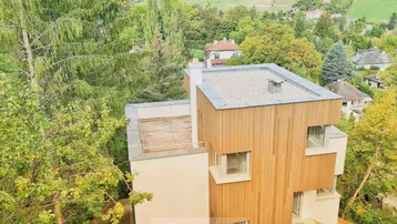 Moderne Architektur mit Holzfassade und Flachdach, eingebettet in grüne Hügellandschaft.
