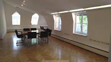 Geräumiges Dachgeschossbüro mit schrägen Wänden, Holzboden und einem großen Konferenztisch für Besprechungen.