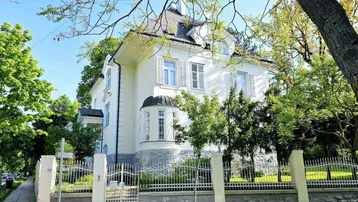 Elegante weiße Villa mit klassischer Architektur und gepflegtem Vorgarten unter blauem Himmel.