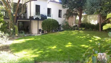 Gepflegter Garten mit großer Rasenfläche und Zugang zu einer Terrasse im Obergeschoss.