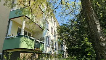 Mehrfamilienhaus mit mehreren Balkonen und grüner Fassadengestaltung, umgeben von Bäumen.