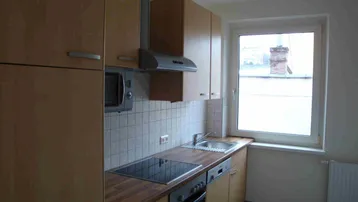 Funktionale Küche mit Holzschränken, Einbaugeräten und einem Fenster mit Blick nach draußen.