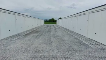 Lange Reihen von weißen Garagenboxen entlang eines Schotterwegs unter bewölktem Himmel mit grüner Landschaft im Hintergrund.
