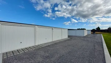 Reihe moderner Garagenboxen mit weißen Toren und Schotterzufahrt unter blauem Himmel.
