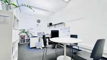 Helles und modernes Büro mit Teppichboden, weißen Wänden und einem runden Besprechungstisch.