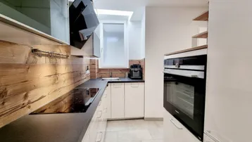 Moderne Küche mit weißen Schränken, Holzwandverkleidung, Induktionskochfeld und Dachfenster.