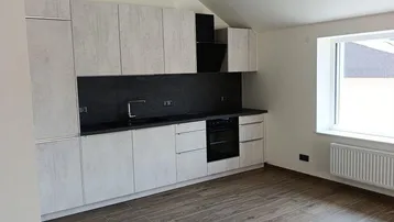 Moderne Einbauküche mit hellen Schränken, dunkler Arbeitsplatte und Holzboden in einem Dachgeschossraum.