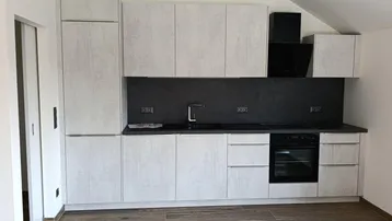 Moderne Einbauküche mit hellgrauen Schränken, dunkler Arbeitsplatte und integriertem Backofen unter einer Dachschräge.