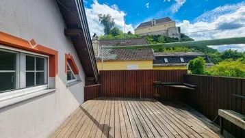 Große Holzterrasse mit Blick auf die umliegende Landschaft und ein historisches Gebäude.