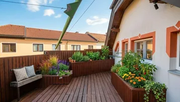Terrasse mit Holzboden, Hochbeeten und Sitzbank, umgeben von Pflanzen und mit Blick auf die Umgebung.