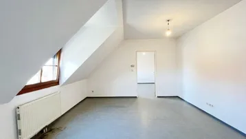 Heller Dachraum mit schrägen Wänden, einem Fenster und einem Heizkörper, bereit zur individuellen Gestaltung.