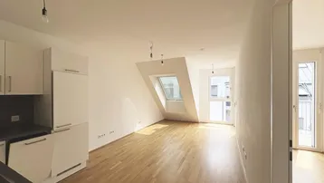 Heller Wohn- und Kochbereich mit Dachschräge, Holzboden und Zugang zu einem Außenbereich.