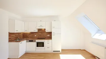 Helle Küche im Dachgeschoss mit weißen Schränken, Holzrückwand und Parkettboden.