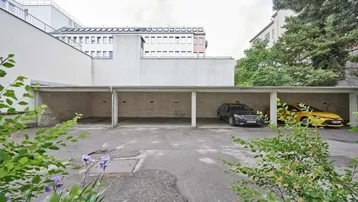 Überdachte Parkplätze im Freien mit zwei Autos und umliegenden Gebäuden.
