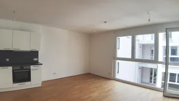 Heller Wohn-Essbereich mit integrierter Küchenzeile und Zugang zum Balkon.