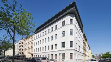 Modernes Eckgebäude mit weißer Fassade und dunklem Dach in einer städtischen Umgebung.