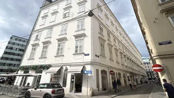 Historisches Eckgebäude in der Stadt mit Geschäften im Erdgeschoss und vielen Fenstern.