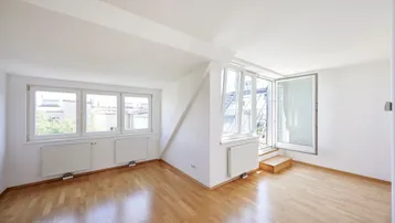 Helles Zimmer im Dachgeschoss mit Holzboden und Zugang zu einem kleinen Balkon.