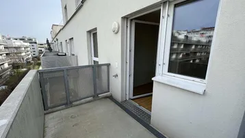 Heller Balkon mit Betonboden und Metallgeländer, bietet einen Blick auf die umliegenden Gebäude.