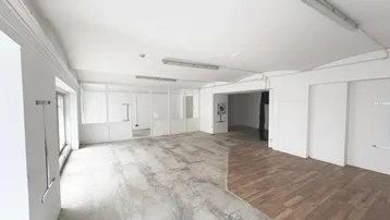 Großer, leerer Raum mit weißen Wänden, teilweise Betonboden und Holzparkett, ideal für gewerbliche Nutzung.