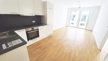Moderne Einbauküche mit weißen Hochglanzfronten und dunkler Arbeitsplatte, offen zum Wohnbereich mit Parkettboden.