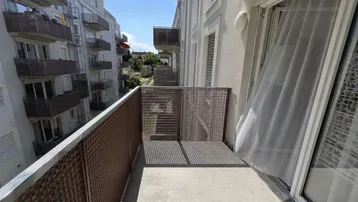 Kleiner Balkon mit Gitterbrüstung und Blick auf umliegende Wohngebäude unter blauem Himmel.