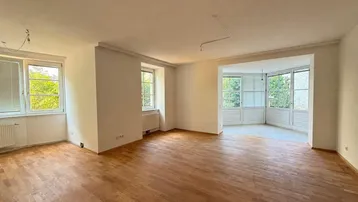 Helles Wohnzimmer mit Parkettboden und einem Erkerbereich mit vielen Fenstern, die viel Licht hereinlassen.