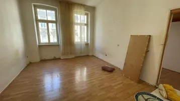 Leerer Wohnraum mit Laminatboden und zwei Fenstern, bereit für eine individuelle Gestaltung.