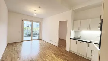 Helles Wohnzimmer mit Parkettboden, Zugang zur Terrasse und integrierter Küchenzeile.