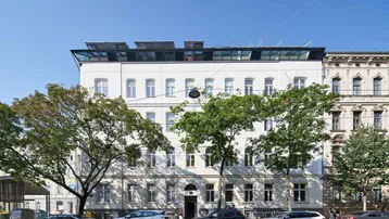Ansicht der modernen Fassade eines Gebäudes mit Solarpaneelen auf dem Dach und Bäumen davor.