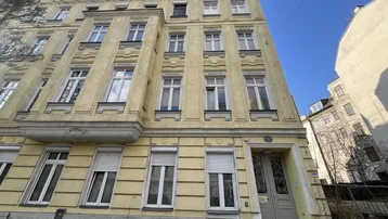 Vorderansicht eines historischen Mehrfamilienhauses mit gelber Fassade und vielen Fenstern.