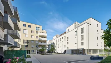 Architekturaufnahme einer modernen Wohnanlage mit Balkonen und gepflastertem Innenhof.