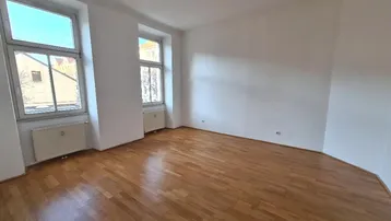 Helles, leeres Zimmer mit Parkettboden und zwei Fenstern, bereit zur individuellen Gestaltung.