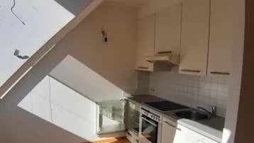 Helle Dachgeschossküche mit Einbaugeräten, weißen Schränken und Holzfußboden, durchflutet von Sonnenlicht.